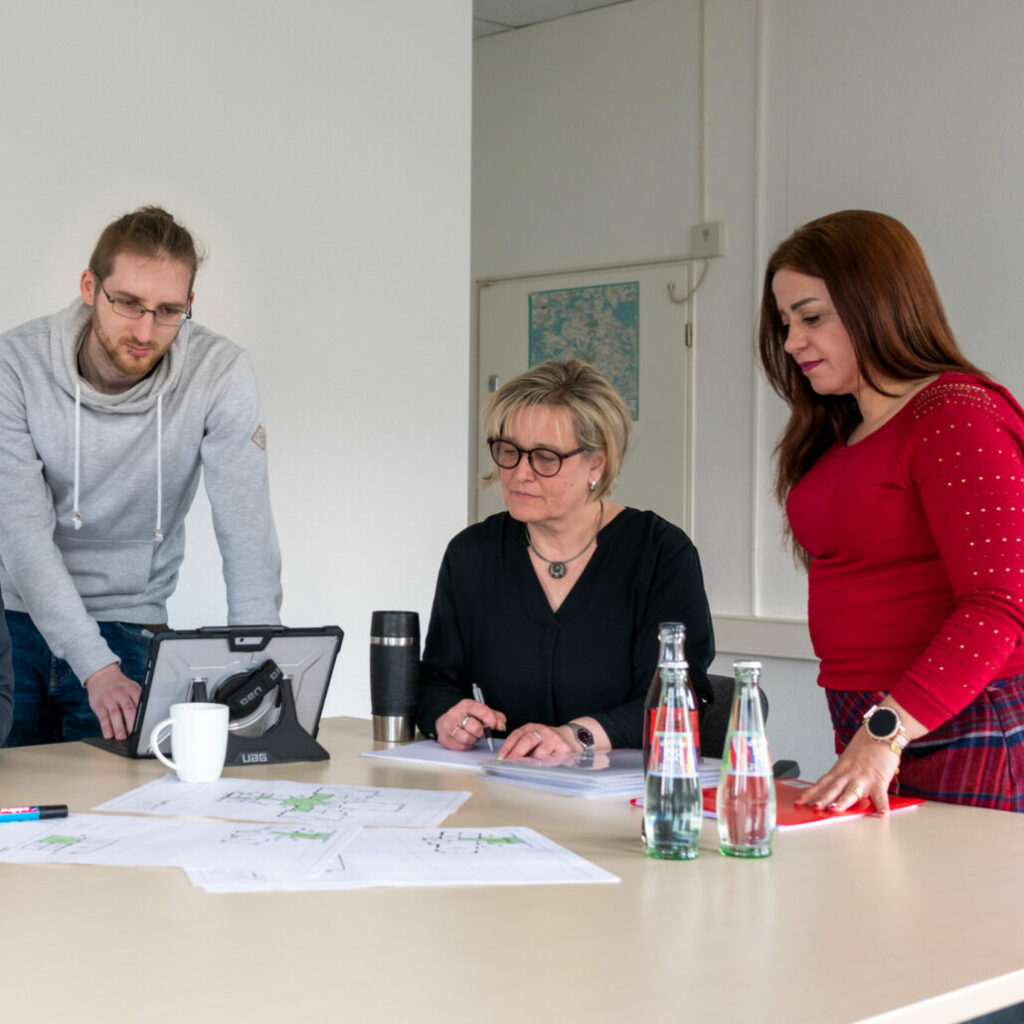 Die Mitarbeiter des BSB-Kröger-Teams besprechen am Tisch Arbeitsunterlagen und Pläne, während sie Dokumente durchsehen und Notizen machen.