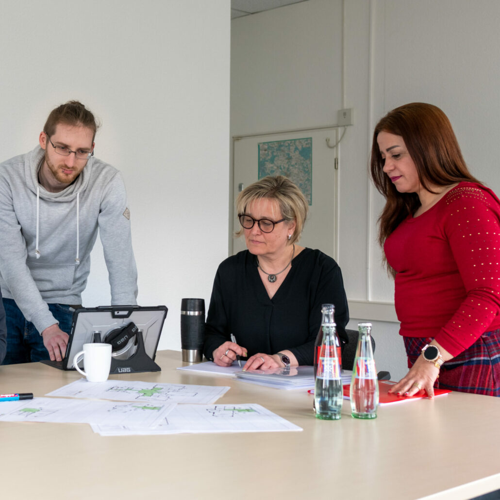 Die Mitarbeiter des BSB-Kröger-Teams besprechen am Tisch Arbeitsunterlagen und Pläne, während sie Dokumente durchsehen und Notizen machen.