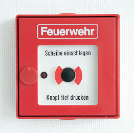 Roter Wand-Feuermelder mit der Aufschrift „Feuerwehr“ und einer Anleitung auf Deutsch: Glas einschlagen und Knopf drücken, um den Alarm auszulösen