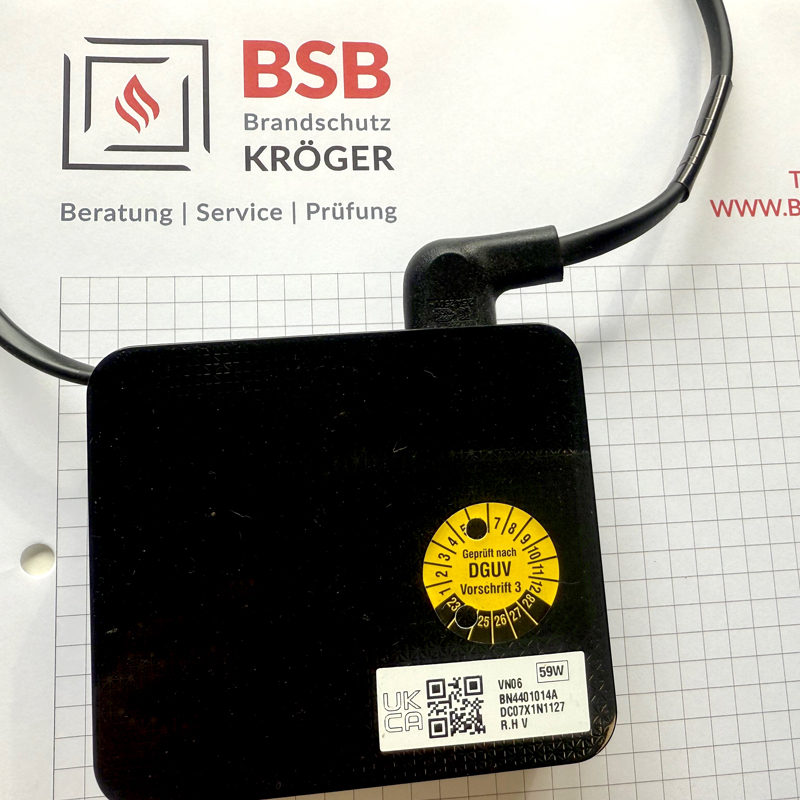 Ein schwarzes Gerät mit einem gelben DGUV-Prüfaufkleber.